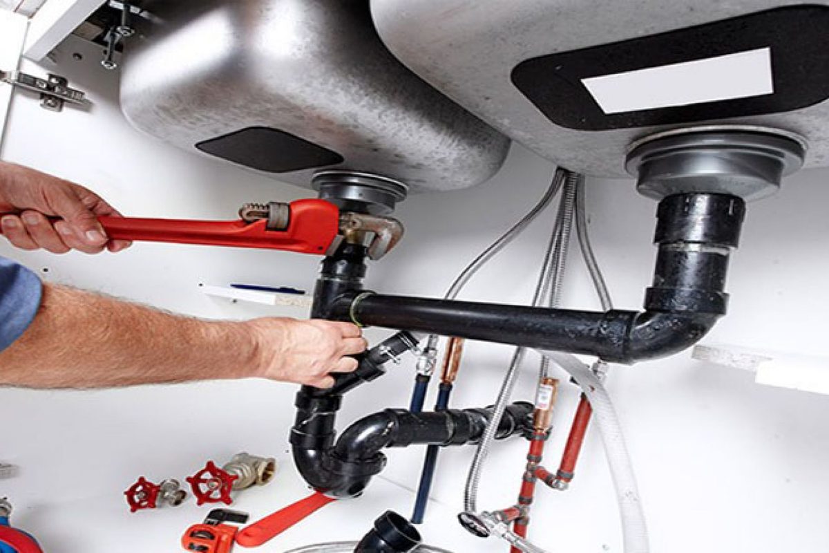 Gasfíter reparando cañerías bajo un lavaplatos